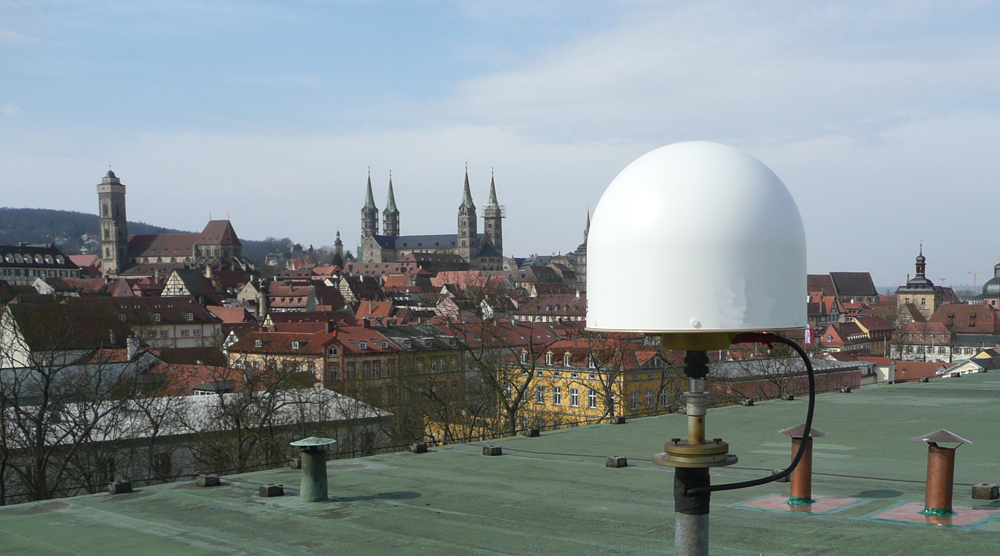 SAPOS-Referenzstationsantenne auf dem Dach der Bamberger Flurbereinigungsbehörde vor Stadtpanorama mit Bamberger Dom.